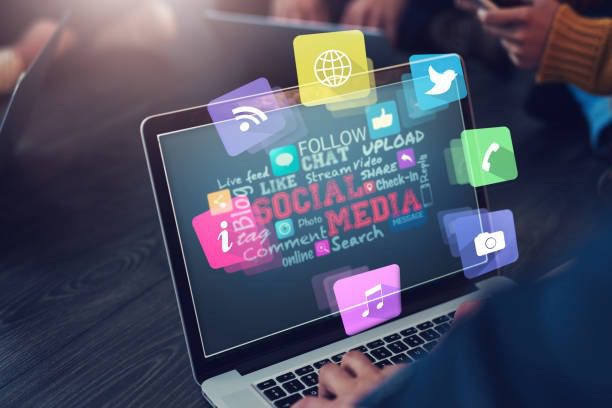 Person using a laptop with floating social media symbols, representing online networking and content sharing.