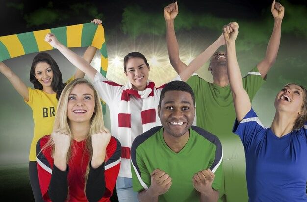Group of diverse soccer fans cheering with raised fists, wearing colorful jerseys and scarves in a stadium setting.